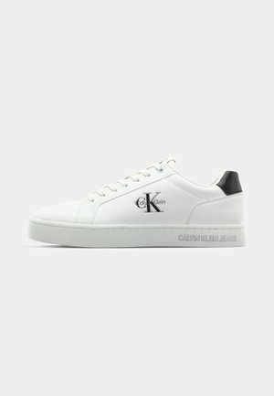 Witte leren sneaker met een gladde textuur, voorzien van een zilveren "CK"-logo aan de zijkant en een zwarte hielaccent. "CALVIN KLEIN JEANS" in reliëf op de zool.