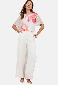 Floral patterned top with sheer, textured sleeves, paired with high-waisted white wide-leg trousers and strappy nude heels.