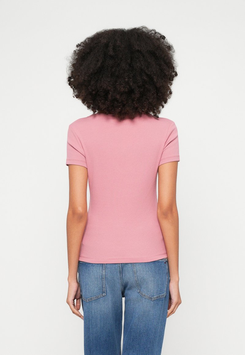 Kurzes pinkes, geripptes T-Shirt mit kurzen Ärmeln, figurbetontem Schnitt und feiner Textur, kombiniert mit blauen Jeans mit Gesäßtaschen.