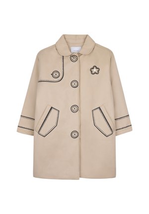 Manteau beige avec des boutons à contour noir, un patch fleur sur la poitrine, des détails de poche et de manches cousus en noir, et un col arrondi.