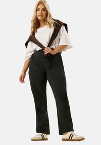 Svarta högmidjade jeans med framfickor, ihop med en vit oversized t-shirt och en brun tröja som hänger över axlarna. Beiga sneakers.