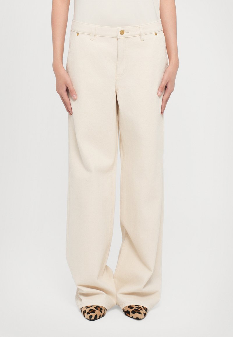 Beige wide-leg trousers with a button closure and front pockets. Fabric appears smooth with a slight texture, paired with leopard print shoes.