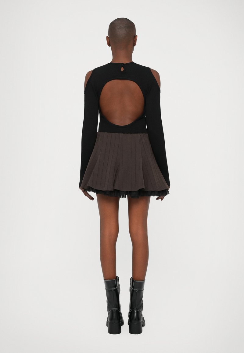 Zwarte lange mouwen top met een open rug, gecombineerd met een geplooide bruine rok met een gelaagde zwarte tule onderrand. Zwarte enkellaarsjes.