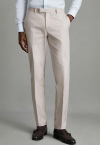 Pantaloni bej, croiți pe corp, cu fit slab, realizați dintr-un material neted. Au bucle pentru curea și o față netedă. Purtați cu pantofi eleganți maro închis.