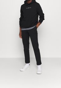 Felpa nera con tasca anteriore e testo bianco, abbinata a pantaloni neri e sneaker bianche. Design moderno con vestibilità comoda.