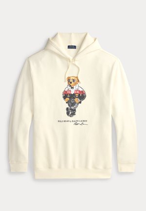 Sweat à capuche couleur crème avec un motif représentant un ours portant des lunettes de soleil et une veste sportive, étiqueté "Polo Bear by Ralph Lauren."