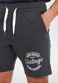 Grey shorts made of soft fabric with a white drawstring. Features a circular graphic print that includes "Vintage" and "Built in Blue."