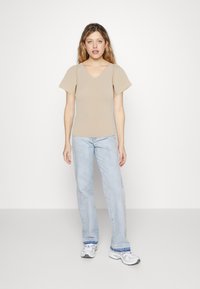 Beige V-hals topp med korte fladderermede ermer, paret med lyseblå rette jeans og hvite joggesko. Glatt tekstur, uformell stil.