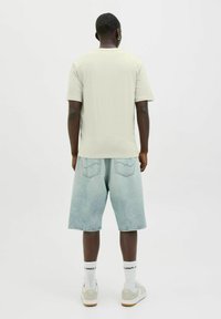 Lichtgrijs T-shirt met korte mouwen, gecombineerd met lichtblauwe denimshorts. Opvallende kenmerken zijn een ontspannen pasvorm en witte sportkousen met lettering.