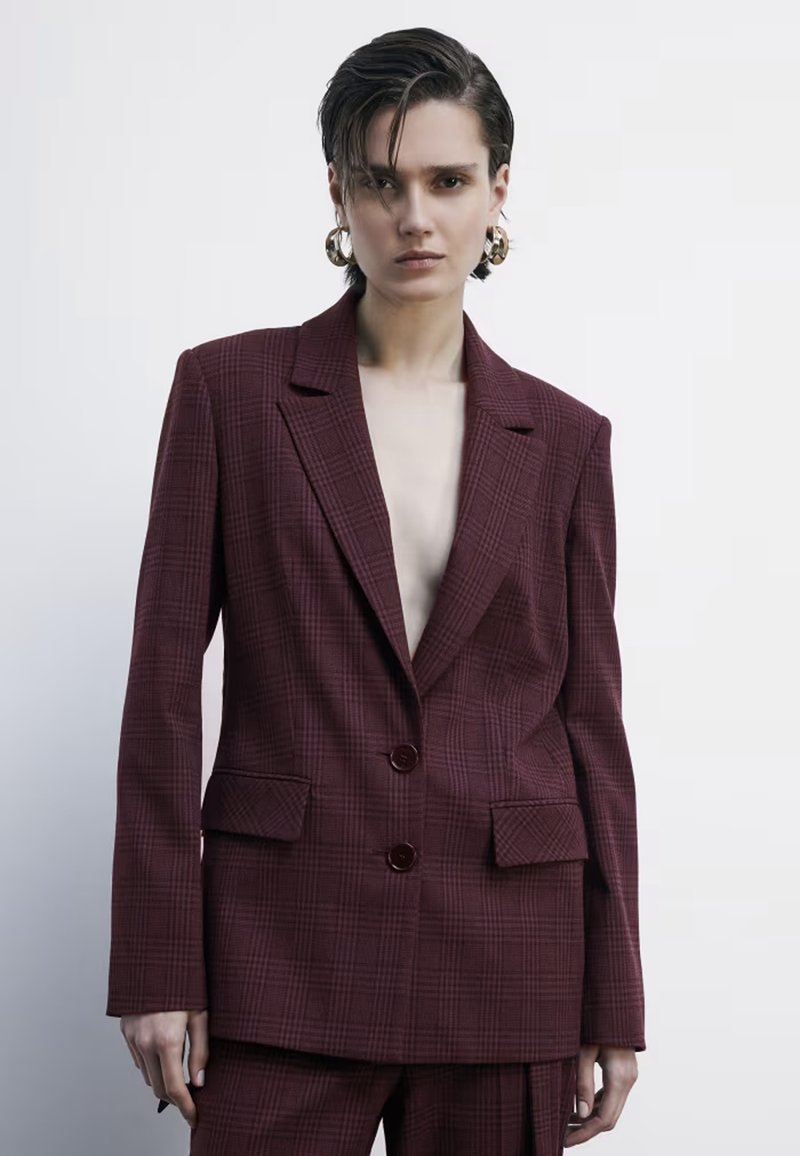 Blazer a quadri bordeaux con revers a punta, due bottoni e tasche frontali. Il tessuto ha una finitura texturizzata, che conferisce una silhouette strutturata.
