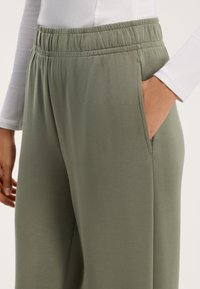 Pohodlné olivově zelené kalhoty volného střihu vyrobené z měkké látky, s elastickým pasem a bočními kapsami. Hladká textura, minimalistický design.