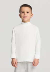 Biała koszulka z długim rękawem i golfem wykonana z miękkiego, lekkiego materiału, zestawiona z jasno szarymi dresowymi spodniami. Prosty design, bez wzorów czy akcentów.