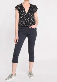 Blouse noire à motifs floraux avec des manches courtes à volants et un décolleté en V profond, assortie à un pantalon capri marine et des baskets métalliques à brides.