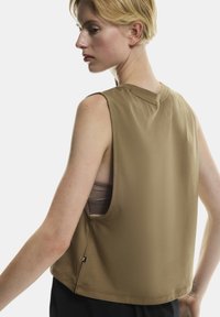 Bezrukávový hnedý top vyrobený z hladkej látky s okrúhlym výstrihom a voľným strihom. Obsahuje bočné otvory a malé logo na leme.