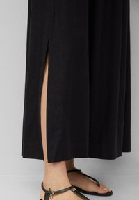 Black maxi dress with a side slit, made of lightweight fabric. Features a straight cut and is paired with black strap sandals.