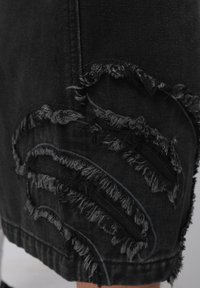 Pantalones cortos de mezclilla negra con detalles deshilachados en patrones de olas, con hilos grises contrastantes que crean textura e interés visual.