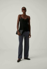 Black satin camisole with lace trim, loose gray trousers, and black clutch. Model wearing dark sunglasses and flat black shoes.