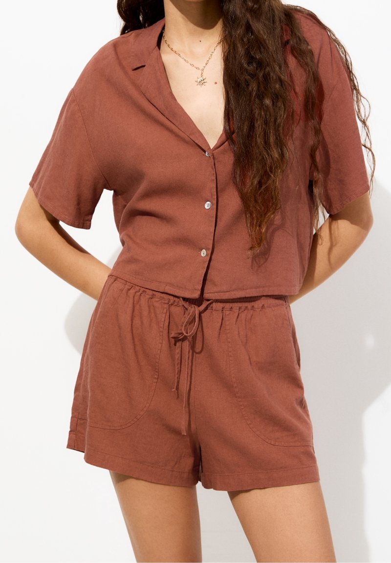 Chemise courte en lin marron avec manches courtes et boutons, associée à un short taille haute assorti doté d'une ceinture élastique et de poches.