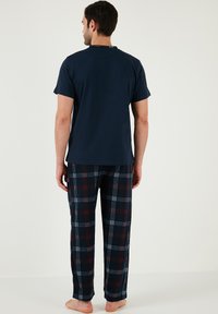 Tricou bleumarin cu mânecă scurtă, asortat cu pantaloni de lounge în carouri, cu accente roșii și albe pe un fond întunecat, din material moale de bumbac.