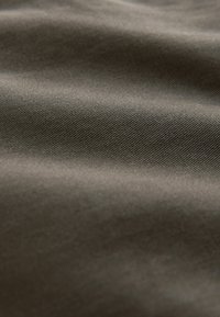 Material texturat în verde măslinie închis, având o suprafață netedă cu modele de țesătură diagonale și variații subtile de dimensiune.