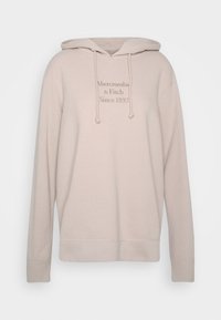 Sweat à capuche beige avec une poche kangourou à l'avant, un cordon de serrage au niveau de la capuche, des poignets côtelés et un logo de marque brodé dans une teinte plus claire. Texture de tissu douce.