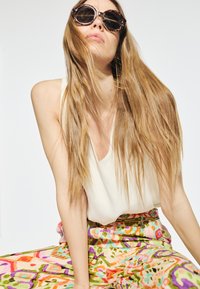 Sunglasses med sköldpaddsdesign och stora runda bågar, kombinerade med en vit topp och livfulla, mönstrade vida byxor.