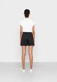 Shorts noirs avec une taille élastique et une coupe décontractée, associés à une chemise blanche à manches courtes. Look décontracté complété par des baskets blanches.