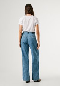 Light blue wide-leg jeans with a textured finish, featuring a mid-rise waist, back pockets, and a black brand label on the waistband.