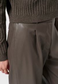 Bruine gebreide trui met geribbelde textuur, gecombineerd met hoge taille, gladde, donkerbruine leren broek met zijzakken.