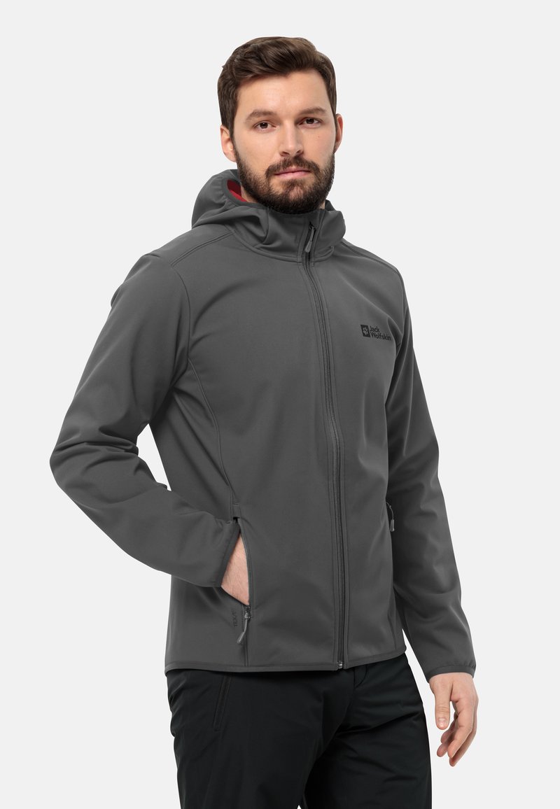 Giacca softshell grigia con cappuccio, chiusura frontale con zip e due tasche laterali. Presenta una texture liscia e un dettaglio logo sul petto.