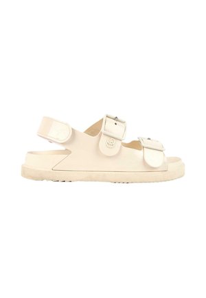 Sandale beige à bout ouvert avec deux boucles réglables sur le dessus et une bride Velcro au talon sur une semelle plate texturée.