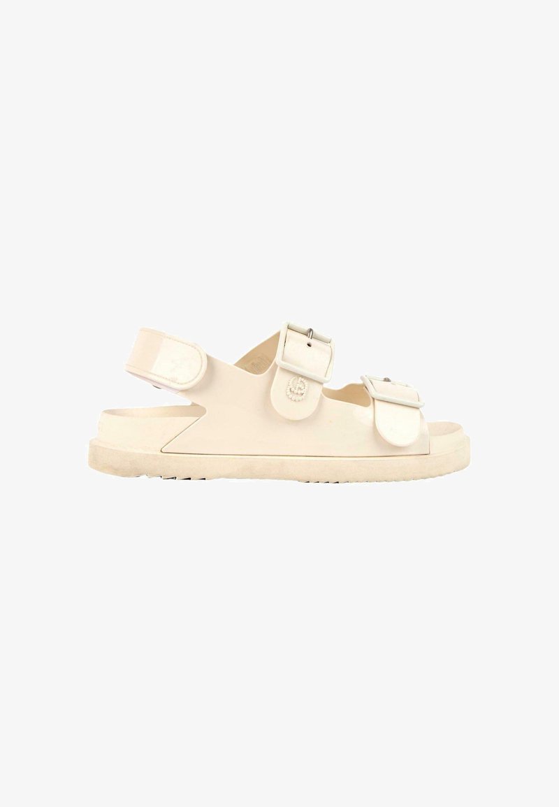 Sandale beige à bout ouvert avec deux boucles réglables sur le dessus et une bride Velcro au talon sur une semelle plate texturée.