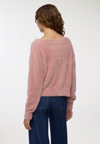 Maglione rosa peloso con vestibilità rilassata, scollatura off-shoulder e maniche lunghe. Abbinato a jeans blu a vita media, per un look informale.