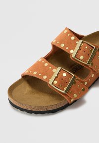 Sandal in suede arancione con due fasce larghe, dettagli in metallo dorato e fibbie metalliche. Sottopiede in sughero. Suola in gomma nera.