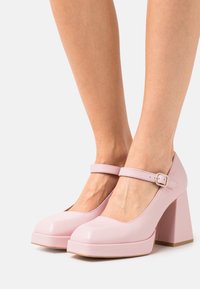 Roze lakleren Mary Jane-hakken met een ronde neus, verstelbare enkelriem en een stevige, vierkante hak. Glad oppervlak en effen kleur.