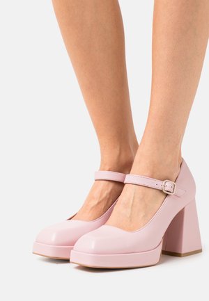 Vaaleanpunaiset kiiltävän nahan Mary Jane -korkokengät, joissa on pyöreä kärki, säädettävä nilkkahihna ja paksu neliönmuotoinen korko. Sileä pinta ja yhtenäinen väri.