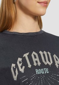 Donkergrijze katoenen T-shirt met een gestructureerde grafische bedrukking in zilver en blauw, met vette, gestileerde letters "GETAWAY ROUTE."