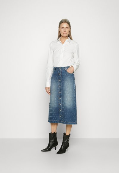 Denim-Midikleid mit Knopfverschluss, Nietenakzenten und einem ausgewaschenen Look. Kombiniert mit einem weißen Hemd und schwarzen Absatzstiefeletten.