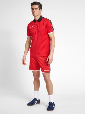 Rode sportpolo met zwarte kraag, gecombineerd met rode shorts met zwarte zijaccenten. Draag het met blauwe sneakers en witte sokken.
