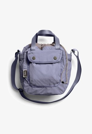 Sac à bandoulière en tissu violet clair avec une poche à rabat à l'avant, des poignées supérieures, une bandoulière ajustable et une fermeture à cordon sur fond blanc.