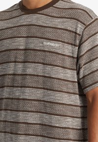 Bruine gestructureerde korte mouwen shirt met een patroon en horizontale strepen van verschillende breedtes, met een ronde hals.