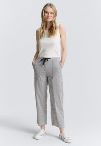 Pantalons rayés, amples, en tissu léger avec une taille élastique et un cordon de serrage. Portés avec un débardeur blanc ajusté et des baskets.