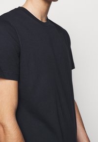 Černé bavlněné tričko s kulatým výstřihem, krátkými rukávy a minimalistickým designem. Tkanina vypadá měkká a hladká.