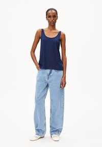 Navyblauw mouwloos topje van zachte stof met een losse pasvorm, gecombineerd met lichtblauwe, wijde jeans. Witte geweven schoenen maken de look compleet.