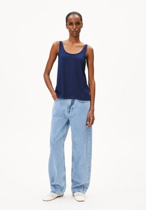 Top senza maniche blu navy, in tessuto morbido con vestibilità rilassata, abbinato a jeans azzurri a gamba larga. Scarpe bianche intrecciate completano il look.