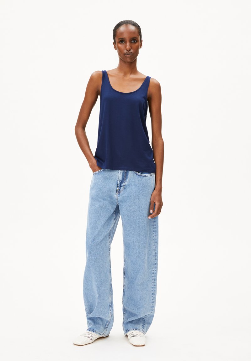 Navyblauw mouwloos topje van zachte stof met een losse pasvorm, gecombineerd met lichtblauwe, wijde jeans. Witte geweven schoenen maken de look compleet.