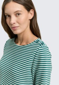 Striped long-sleeve top in teal and cream. Features a crew neck and two decorative buttons at the shoulder. Soft, textured fabric.