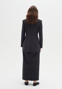 Čierny strihaný oblek s priliehavým blejzrom a dlhou sukňou, vyrobený z hladkého materiálu, so jedným rozparkom a elegantným siluetou.
