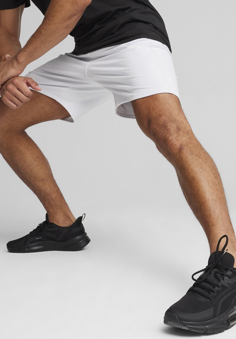 Shorts deportivos blancos con una textura suave y una cintura elástica, combinados con zapatillas negras que presentan una superficie texturizada y cordones.