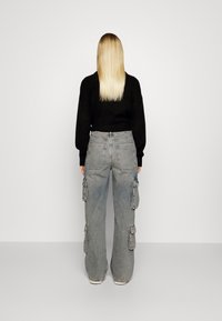 Jeans cargo de cintura alta en denim azul claro, con cuatro grandes bolsillos laterales, un corte holgado y dobladillos deshilachados. Combinados con un suéter negro de punto.